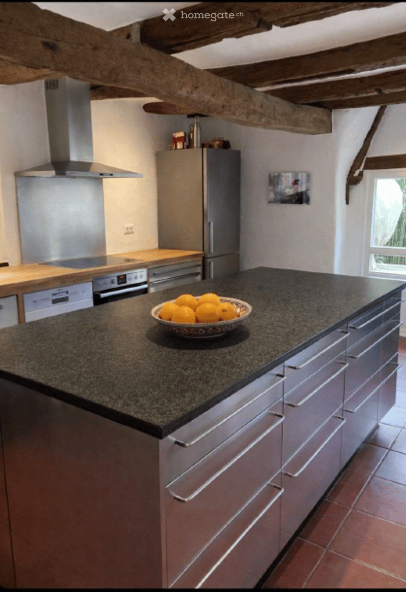 Modern kitchen with stainless steel appliances, granite island, and a bowl of oranges on the counter.
