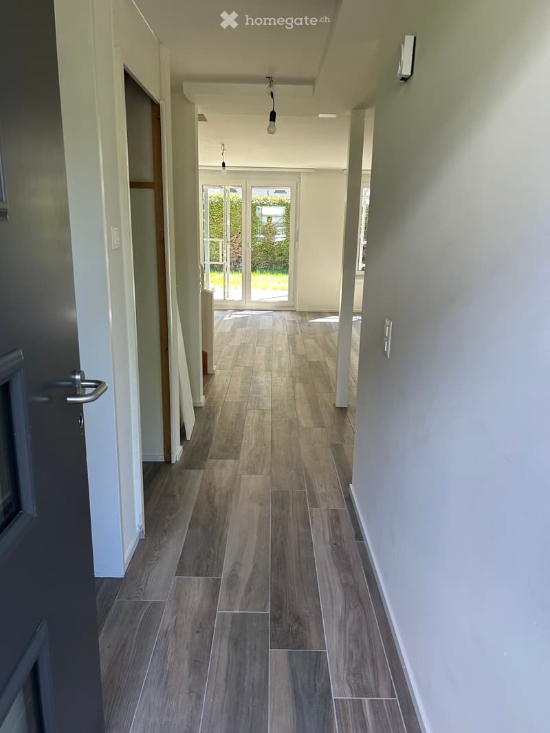Empty hallway with wooden floor, white walls, glass doors, and lights