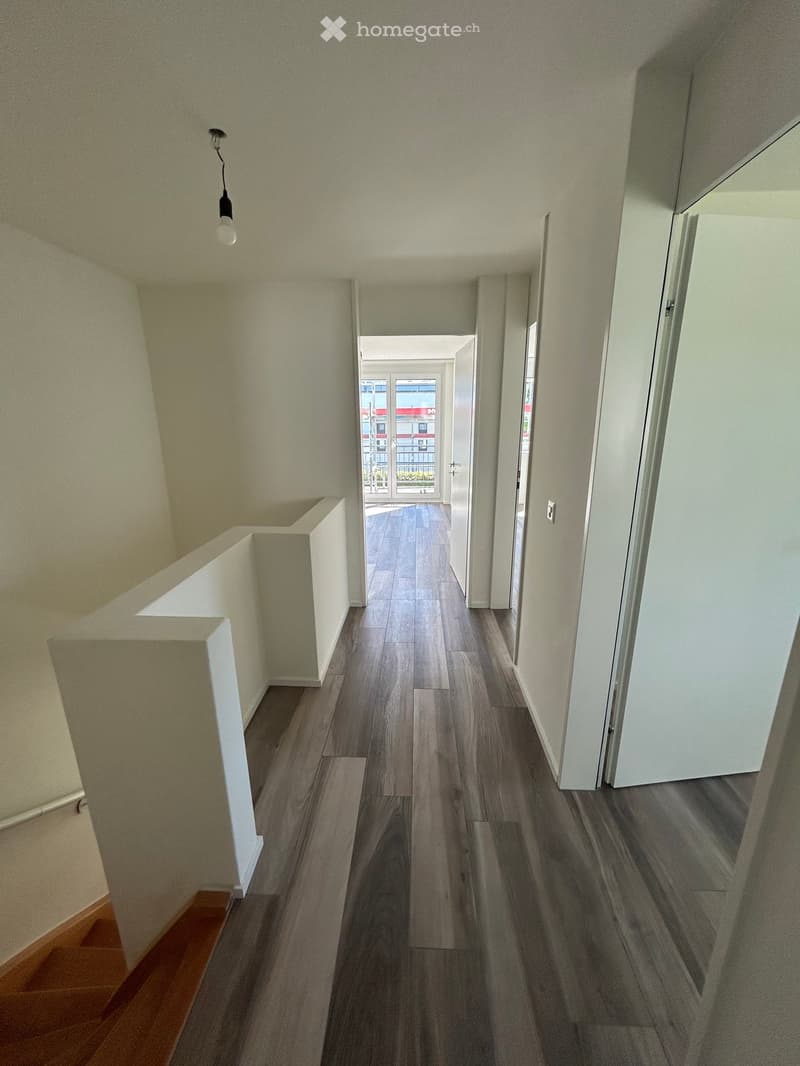 Empty hallway with wooden floor, white walls, white doors, and a staircase.