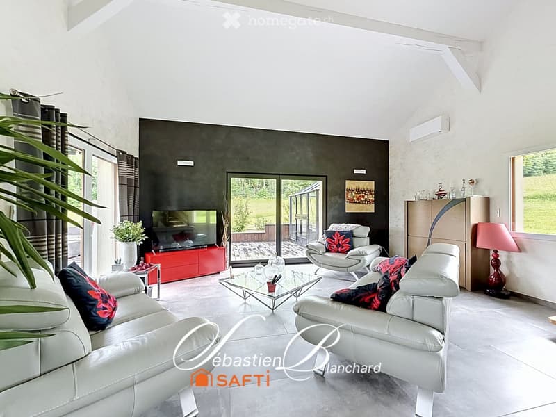 Modern living room with white leather sofas, a glass coffee table, a red TV cabinet, and large windows leading to a patio.