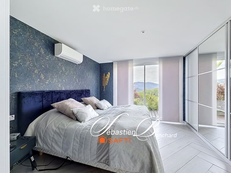 Modern bedroom with a large bed, nightstand, air conditioner, and scenic mountain view through large windows.