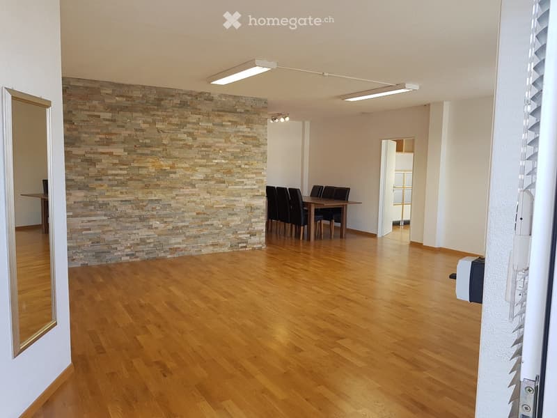 Empty room with hardwood floors, stone wall, table and chairs, ceiling lights, mirror on wall
