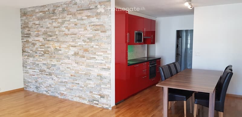 Dining area with dining table and chairs, open plan kitchen with red cabinets, brick wall, wooden floor