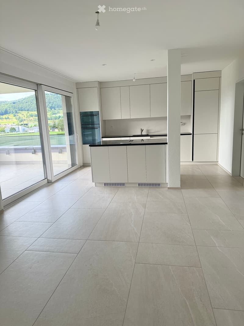 Empty kitchen with white cabinets, a sink, and a built-in oven. Large sliding glass doors open to a view of greenery outside.