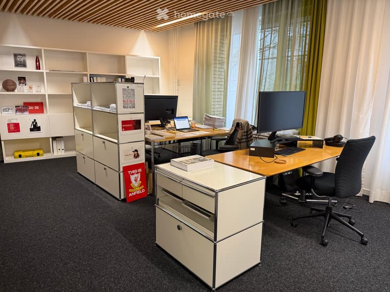 Modern office space with a wooden desk, ergonomic chair, dual monitors, laptop, keyboard, mouse, books, and storage units.