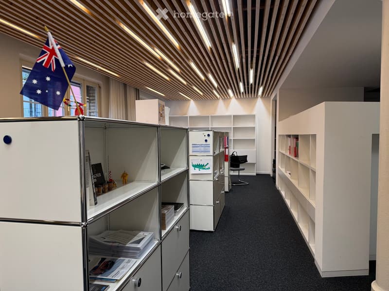 Modern office space with white cabinets, shelves, a chair, and a small Australian flag visible in the background.