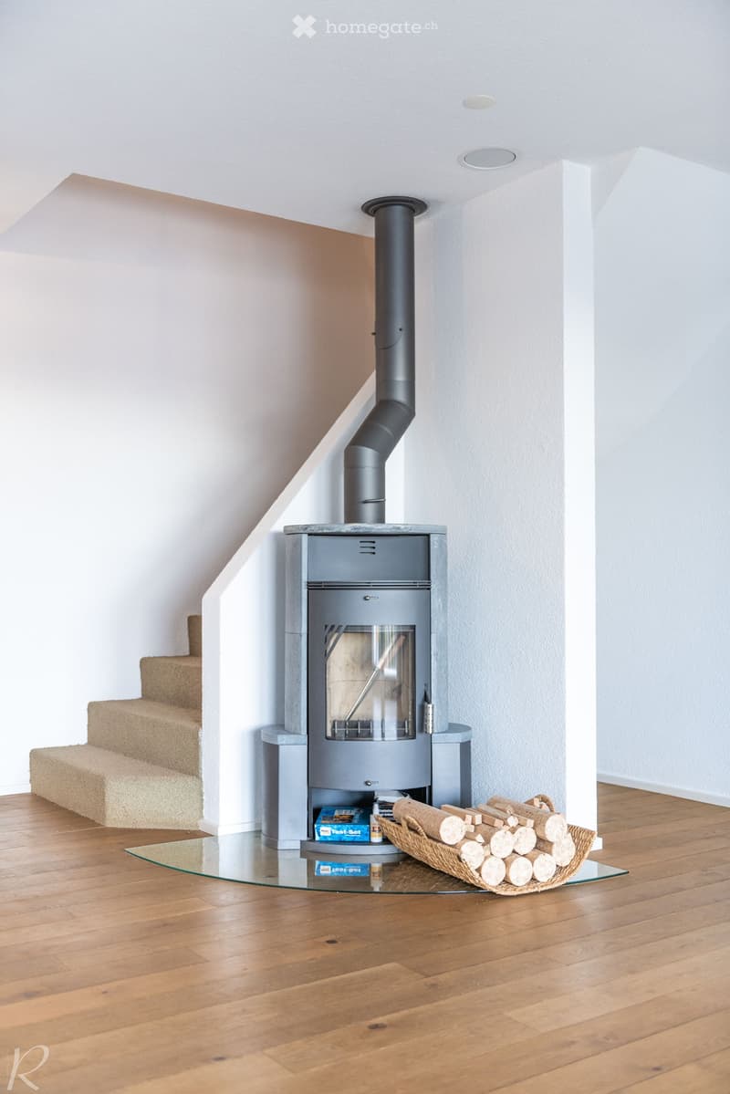 Modern hallway with wooden flooring, a sleek grey wood-burning stove, and a basket of firewood nearby.