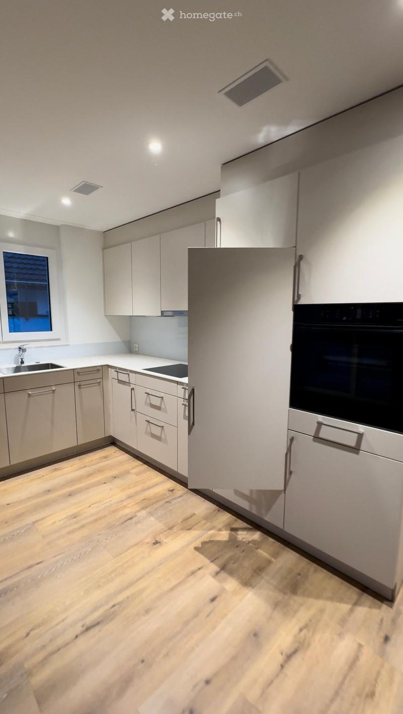 Modern kitchen with light-colored cabinets, wooden flooring, and stainless steel appliances including a sink, faucet, and oven.