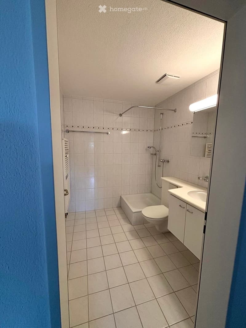 Modern bathroom with white tiles, a bathtub, toilet, sink, and a shower area with a glass enclosure.