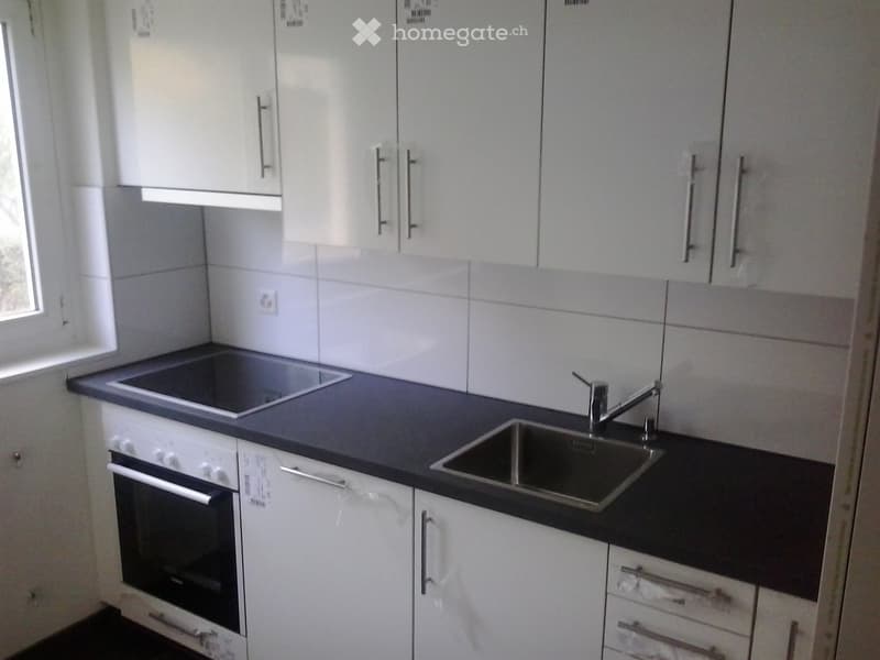 Modern kitchen with white cabinets, black countertops, an oven, a sink, and a faucet.