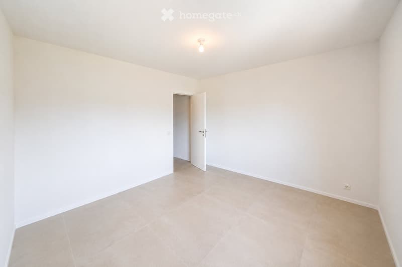 Empty room with white walls, tiled floor, and a single light fixture on the ceiling. An open door leads to another space.
