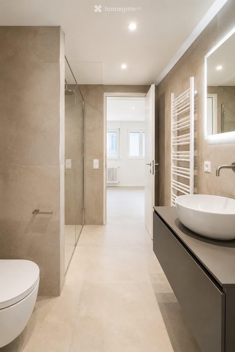 Modern bathroom with beige tiles, a white toilet, a sink with a modern faucet, a large mirror, a glass-enclosed shower, and a towel rack.