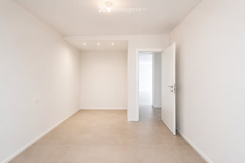 Empty room with light-colored walls, tiled floor, and a single open door leading to another space.