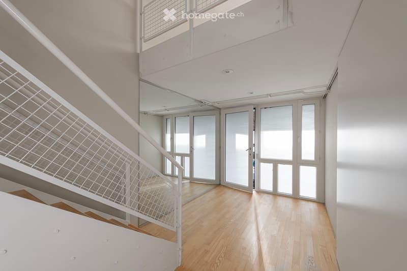Empty corridor with white walls, wooden floor, and a white handrail on the left.
