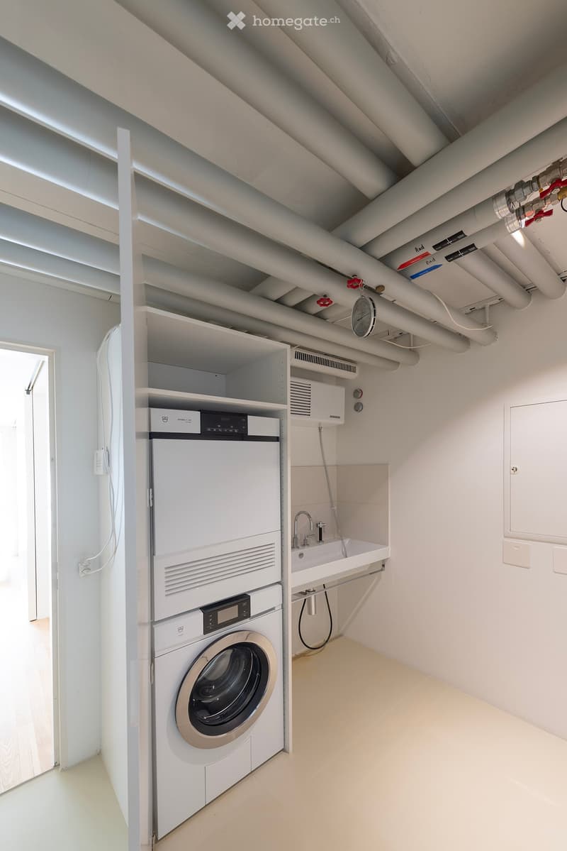 A small laundry room with a washing machine, dryer, sink, and pipes.