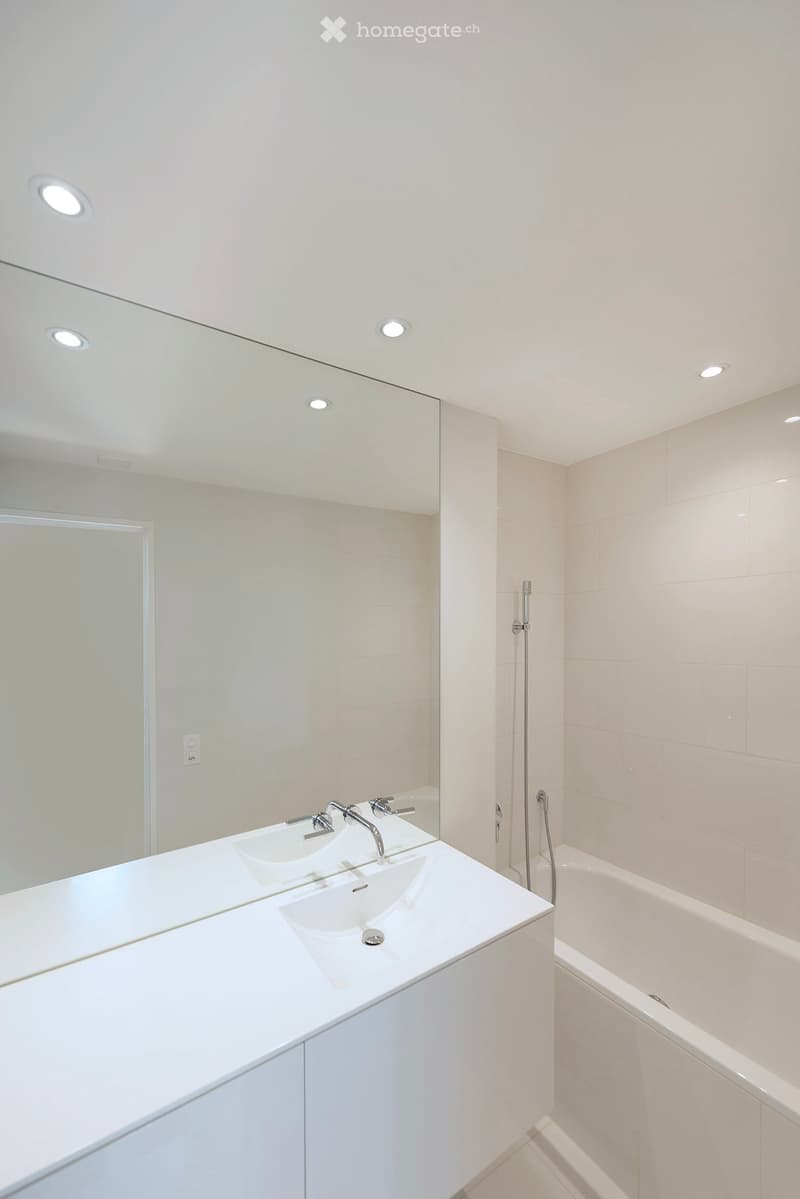 Modern bathroom with a white double sink, large mirror, bathtub, and sleek fixtures.