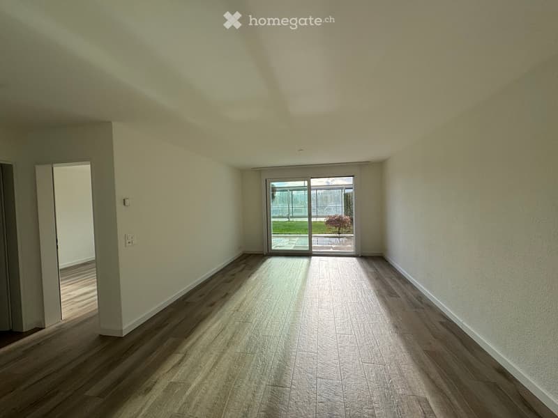 Empty room with light-colored walls, wooden flooring, and a sliding glass door leading to an outdoor area.