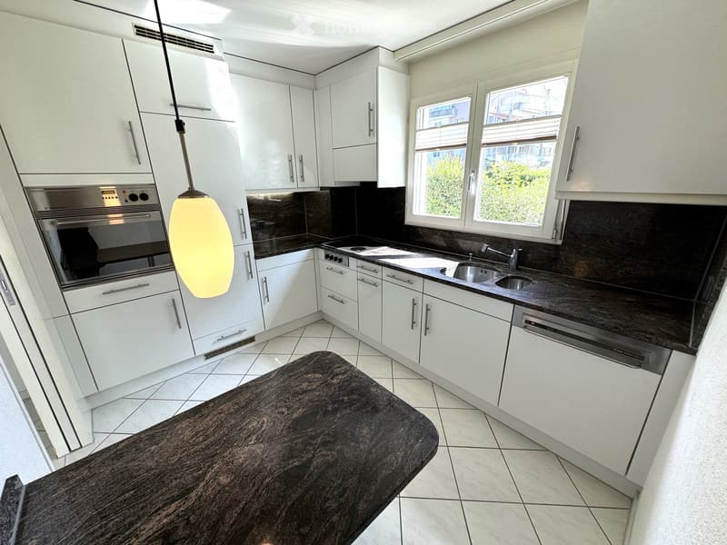 Modern kitchen with white cabinets, stainless steel appliances, dark countertops, and a central island.