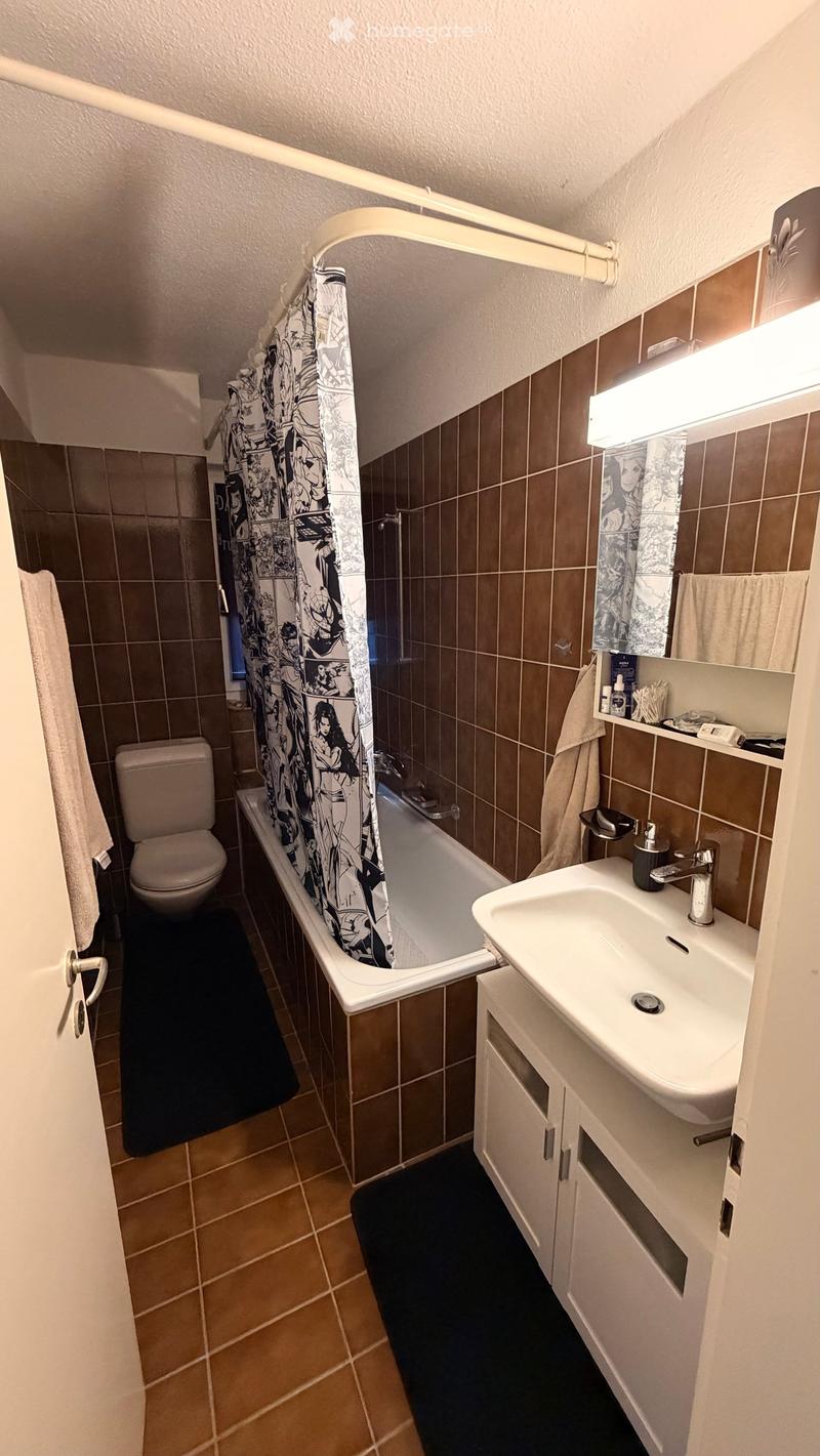Bathroom with a bathtub, toilet, sink, mirror, and cabinet. Features a shower curtain with a comic book design and a towel on the side.