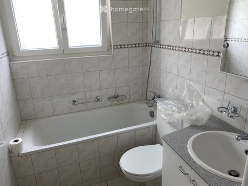 Bathroom with white tiles, bathtub, toilet, sink, mirror, and towel rack.
