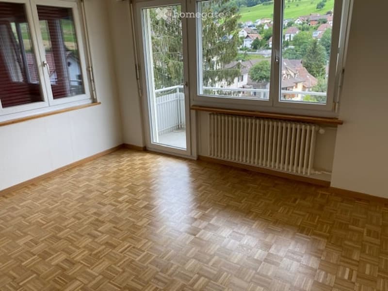 Empty room with wooden parquet flooring, large windows offering a scenic view, and a radiator under one window.