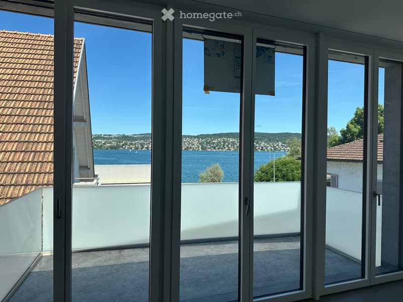 Open balcony with large glass doors leading to a scenic view of a lake and surrounding landscape.