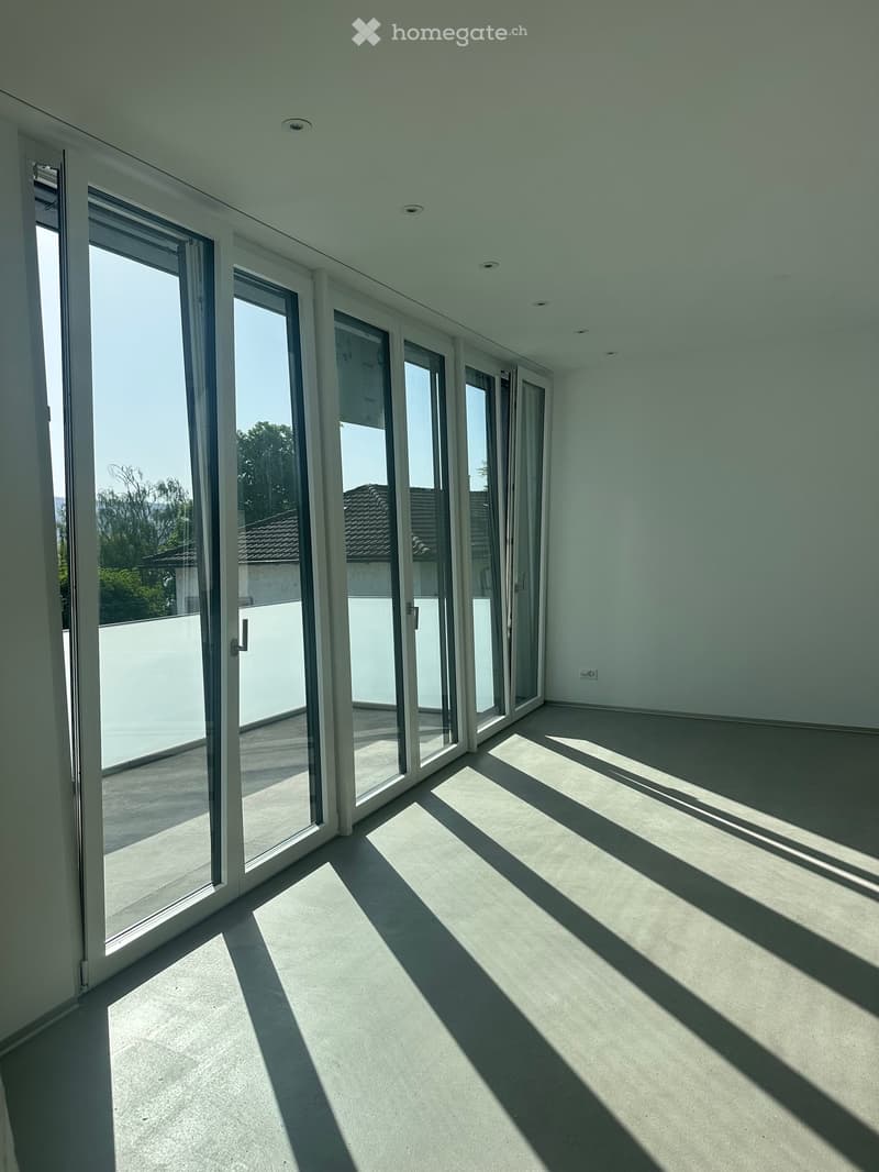 Empty room with large glass sliding doors leading to a balcony, light-colored walls, and a smooth concrete floor.
