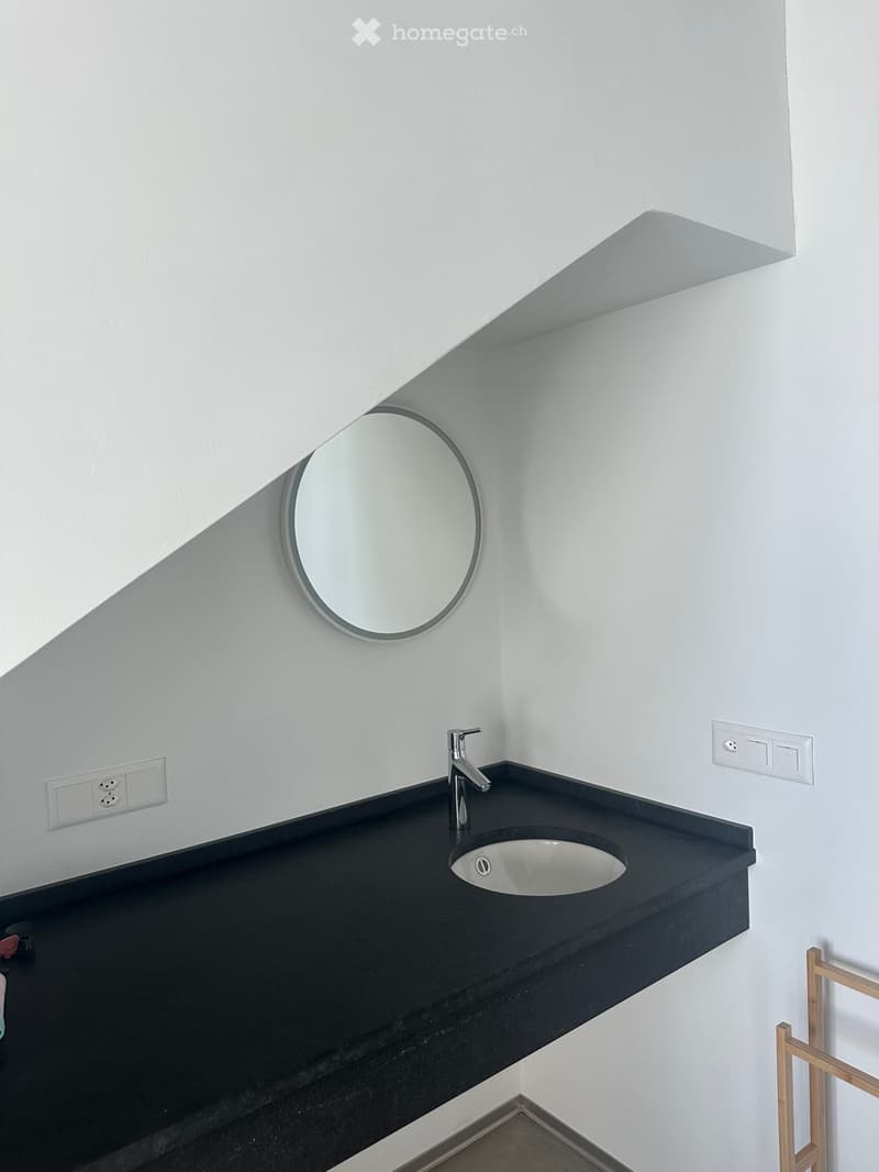 Modern bathroom with a black countertop, white sink, chrome faucet, and round mirror on the wall.