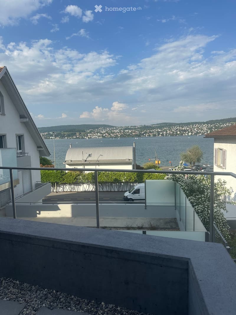 Balcony overlooking a scenic lake with distant cityscape and hills under a partly cloudy sky.