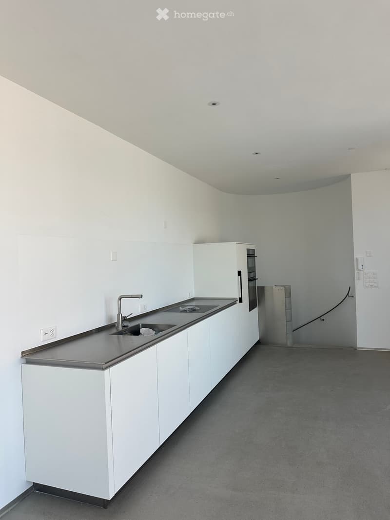 Modern kitchen with white cabinets, stainless steel sink, faucet, and built-in oven. The space is clean and minimalistic with a concrete floor.