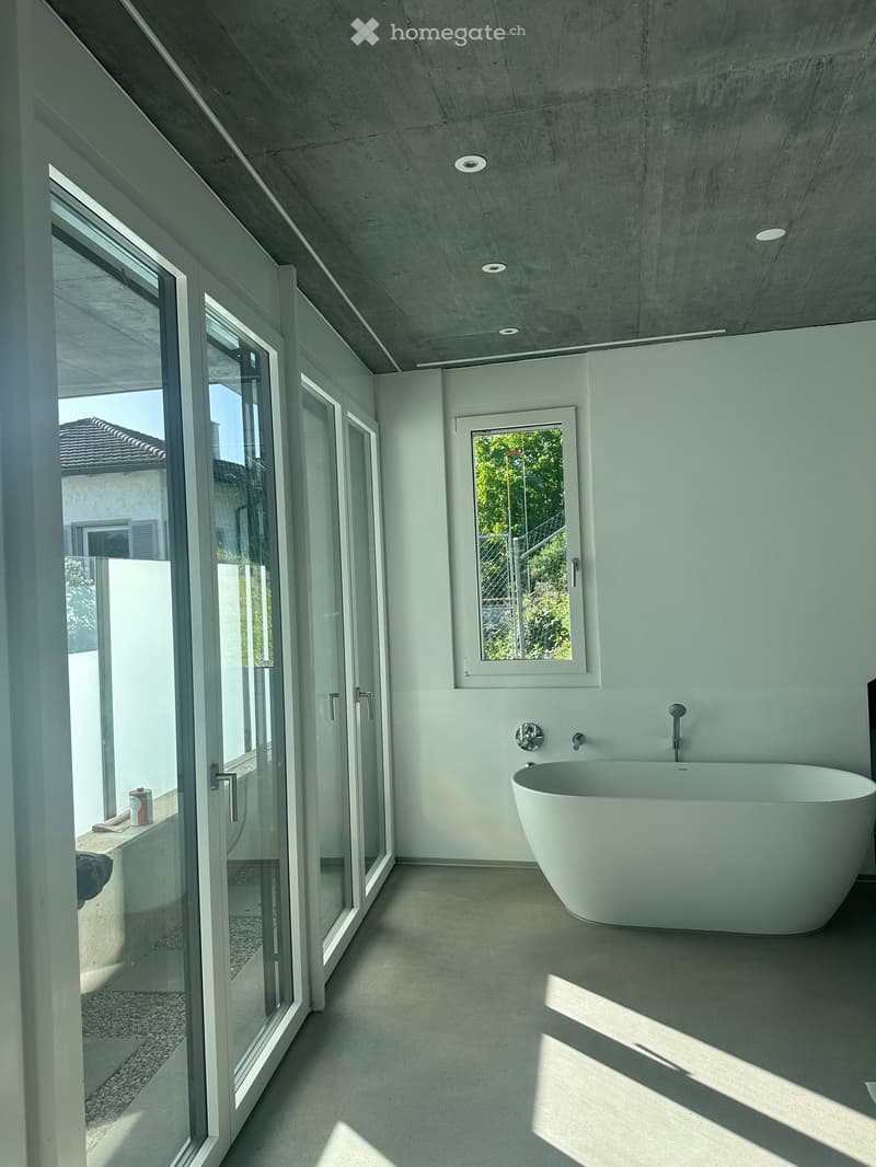 Modern bathroom with a large, freestanding bathtub, sleek white walls, and large glass doors leading to an outdoor area.