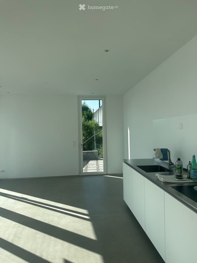 Modern kitchen with white cabinets, dark countertop, and a sink area. Sunlight streams in from a large sliding door leading to an outdoor area.