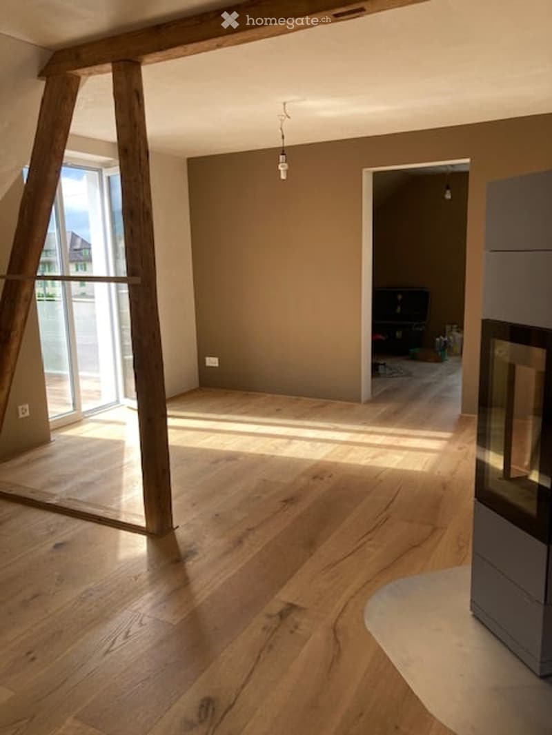 Empty room with wooden flooring, large windows, and exposed wooden beams. No furniture or equipment present.