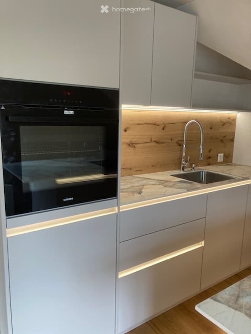 Modern kitchen with sleek grey cabinets, a built-in oven, a wooden backsplash, and a stainless steel sink with a modern faucet.