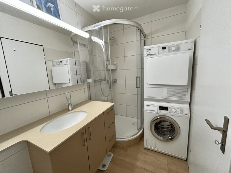 Bathroom with shower cubicle, sink, cabinets, washing machine, and dryer