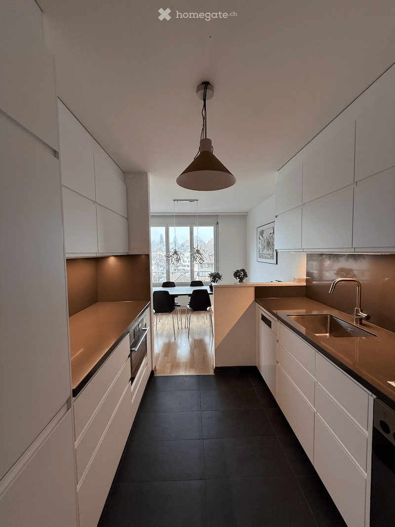 Modern kitchen with white cabinets, black tiles, a central island, gas stove, oven, dishwasher, and a hanging light fixture