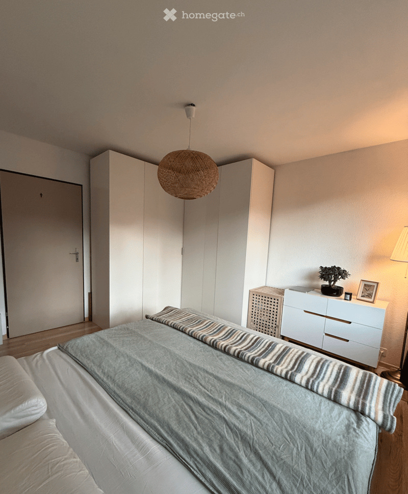 bedroom with bed, white storage units, white wardrobe, white flooring, lamp, small table, potted plant
