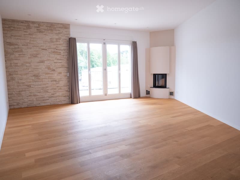 Empty room with wooden flooring, large windows, and a fireplace on the right side.