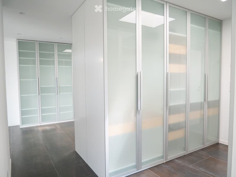 Modern hallway with glass-paneled doors and a polished tile floor, featuring recessed lighting and white walls.