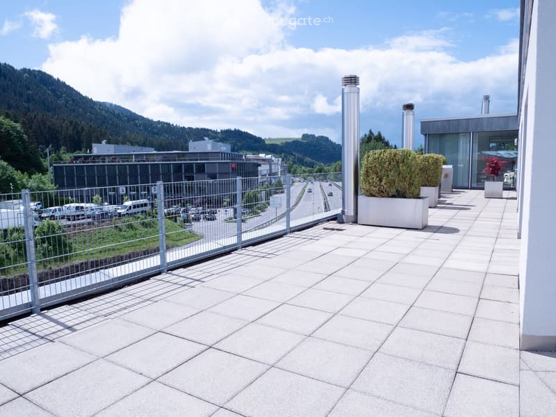Balcony with tiled floor, metal railing, potted plants, and a view of a parking lot and surrounding landscape.