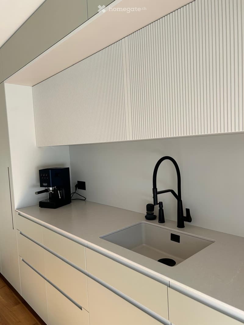 Modern kitchen with light-colored cabinets, a stainless steel sink, a black faucet, and a coffee machine on the counter.