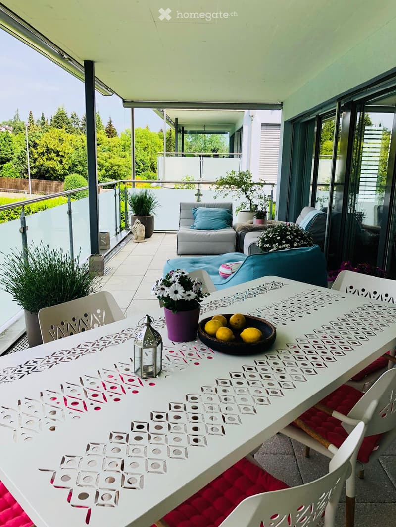 Balcony with a white table, chairs, sofa, flower pots, and decorative items.