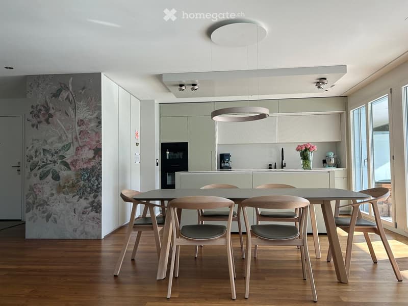 Modern kitchen with light green cabinets, a round pendant light, a dining table with six chairs, and a vase of flowers on the counter.