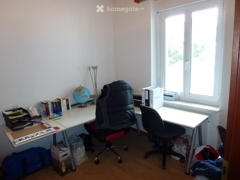 A well-lit study or office space with a large window, two desks, two chairs, a globe, books, a laptop, and a lamp.