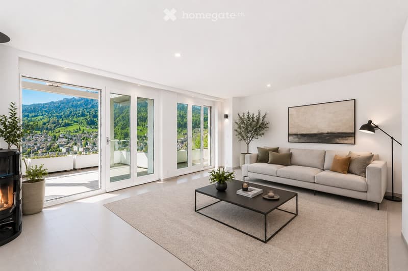 Modern living room with large windows offering a scenic view, a grey sofa with throw pillows, a black coffee table, a floor lamp, and a fireplace.