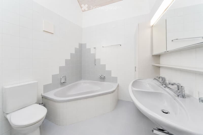 Modern bathroom with white tiles, a bathtub, a toilet, a double sink, and a mirrored cabinet.