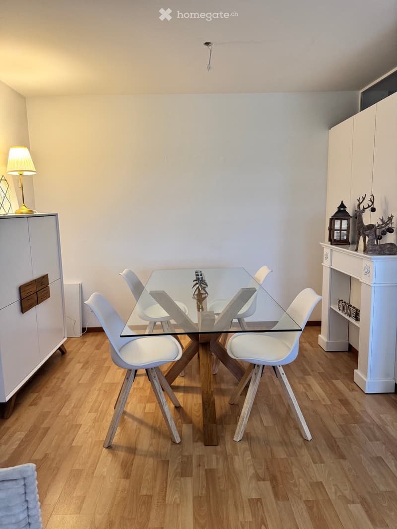 Modern dining area with a glass table, white chairs, wooden flooring, and decorative items including a lamp and a sculpture.