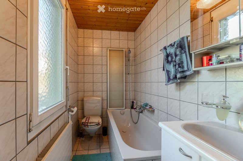 Bathroom with tiled walls and wooden ceiling, featuring a bathtub, toilet, sink, mirror, and towel hanging on the wall.