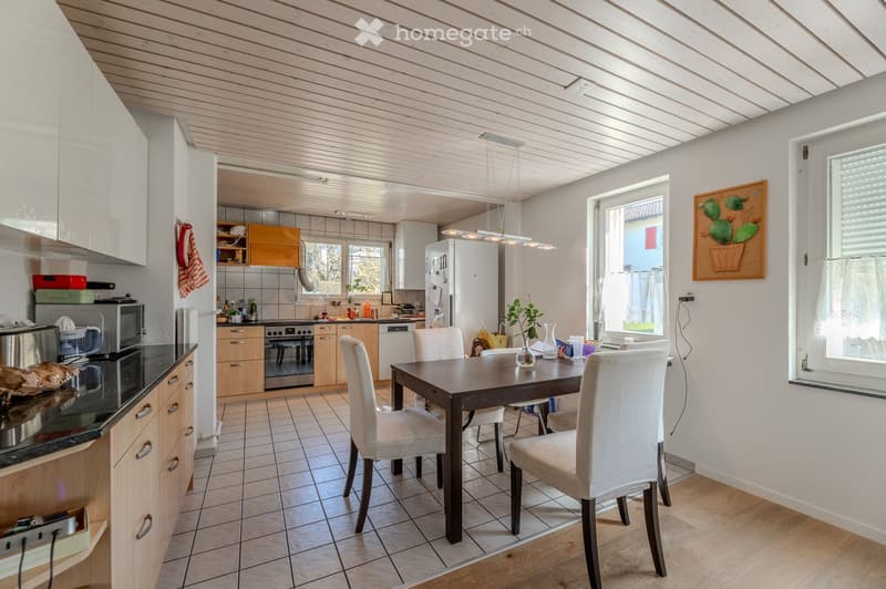 Bright, open-plan kitchen and dining area with wooden cabinets, stainless steel appliances, a dining table with chairs, and a pendant light fixture.