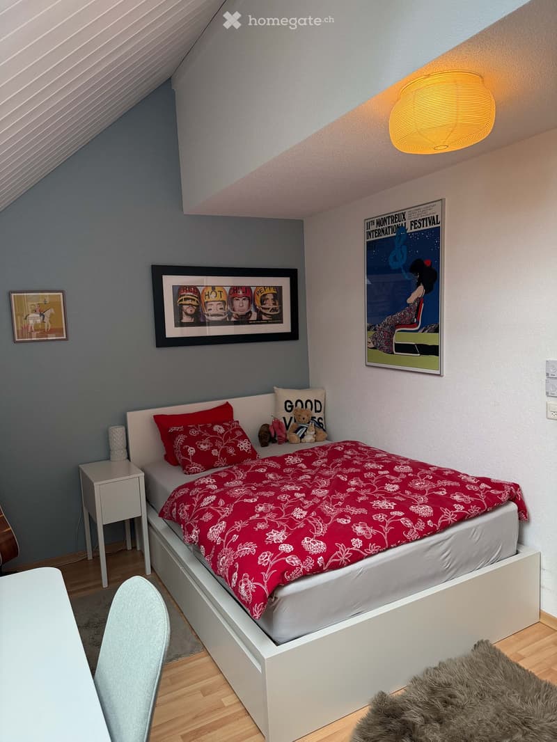 Cozy bedroom with a white bed, red bedding, nightstand, chair, and framed pictures on the walls.